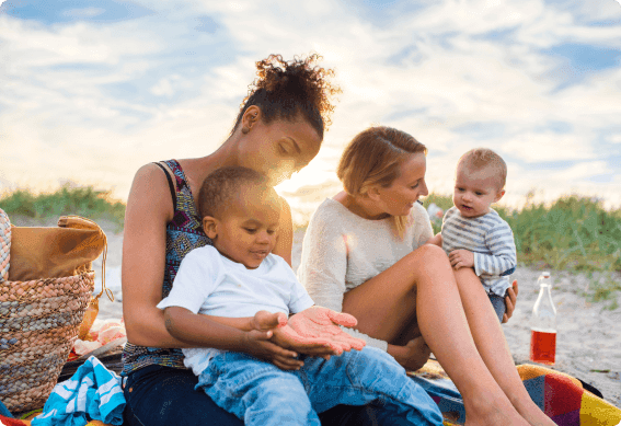 a person and two children sitting on a blanket on a beach