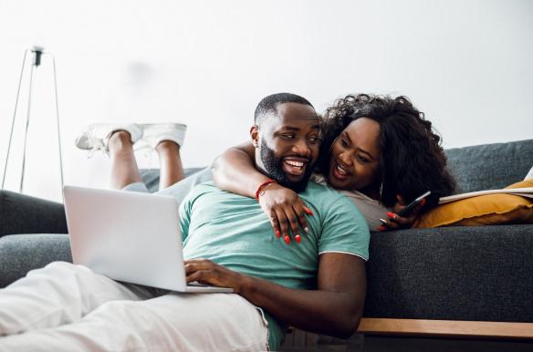 a man and woman laughing while sitting on a couch with a laptop