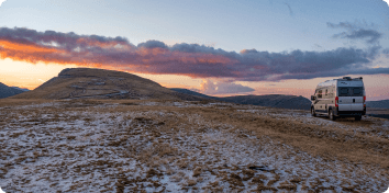 an RV parked on a rocky terrain at sunset