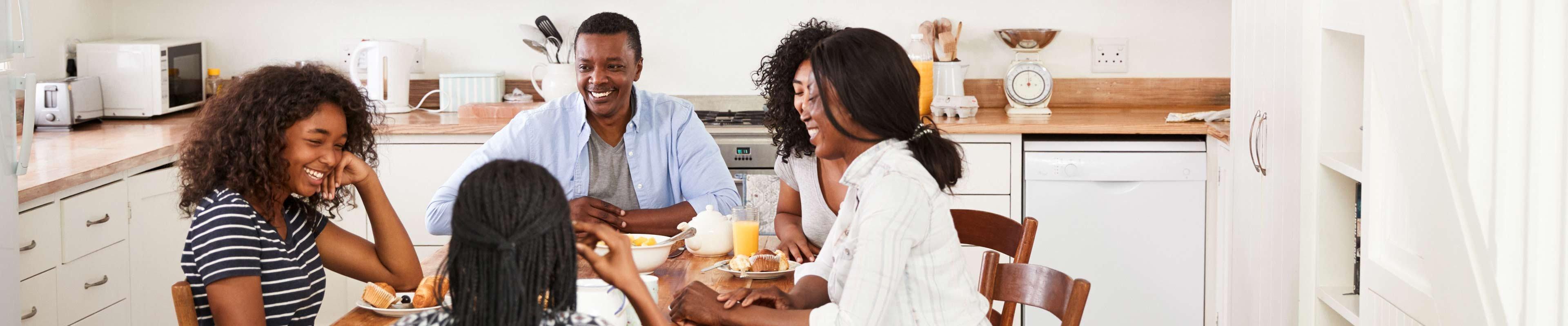 Family of four eating breakfast at the table in their home. 