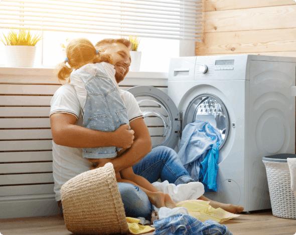 A parent hugging their child while sitting in front of their home dryer.