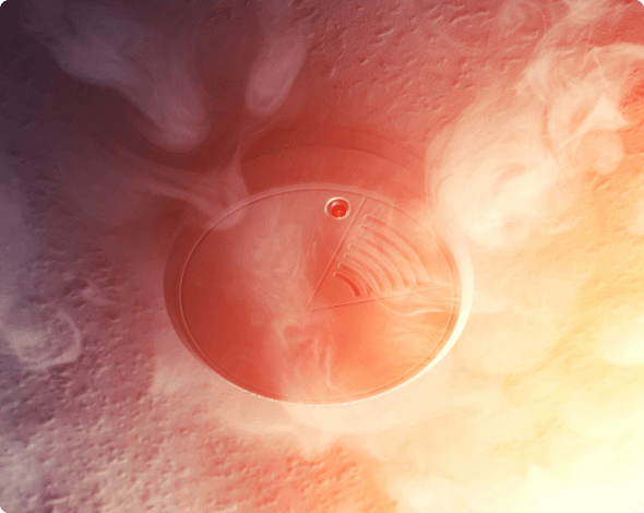 A close-up of a home's smoke alarm, surrounded by smoke. 