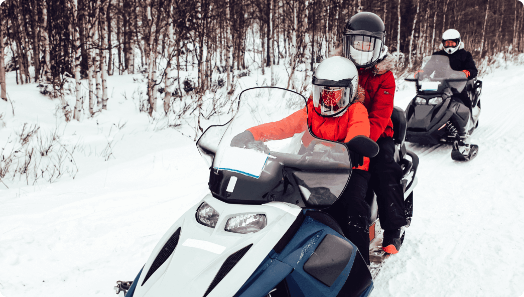 Child driving a snowmobile with a parent